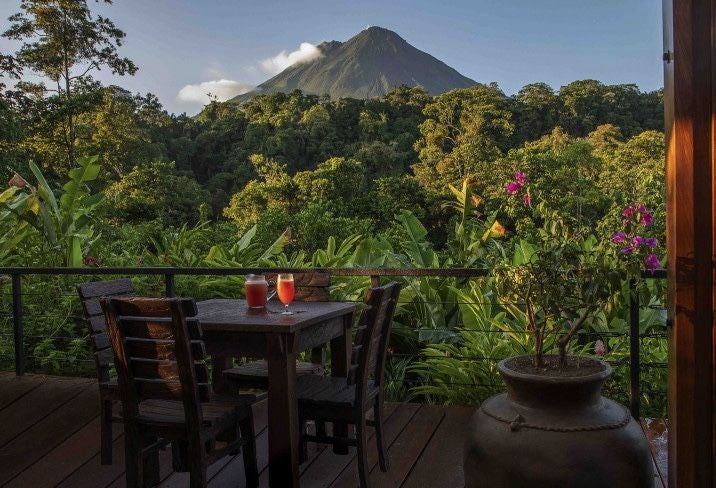 Luxurious hotel room with floor-to-ceiling windows overlooking lush Costa Rican rainforest, featuring modern decor and private balcony