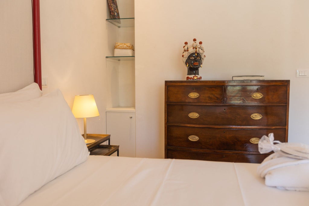 Elegant Sicilian bedroom with soft neutral tones, antique wooden furnishings, plush white linens, and ornate architectural details at luxurious boutique hotel