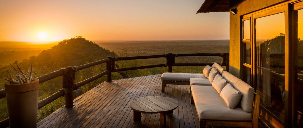 Luxurious hilltop lodge with panoramic glass windows and stone walls perched on dramatic cliffs overlooking African savanna at sunset