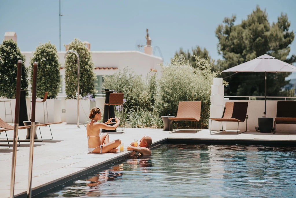 Luxurious seafront hotel with white-washed facade, azure pool, and panoramic Mediterranean views in Talamanca, Ibiza, surrounded by palm trees and elegant design