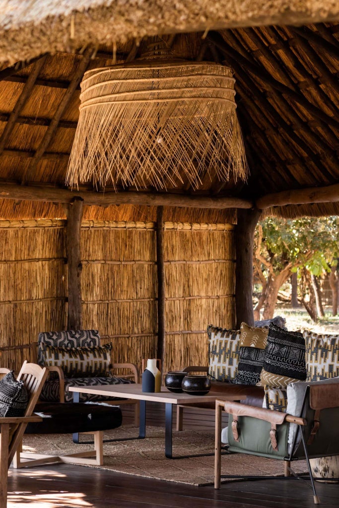 Luxurious safari lodge nestled in lush Zambian wilderness, featuring elegant tented suite with wooden deck overlooking pristine river landscape at sunset