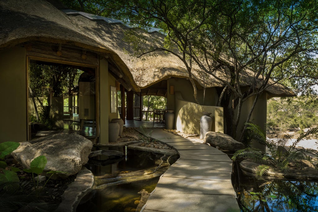 Luxurious safari lodge perched atop granite rocks overlooking African savanna, with infinity pool extending over cliff edge at sunset