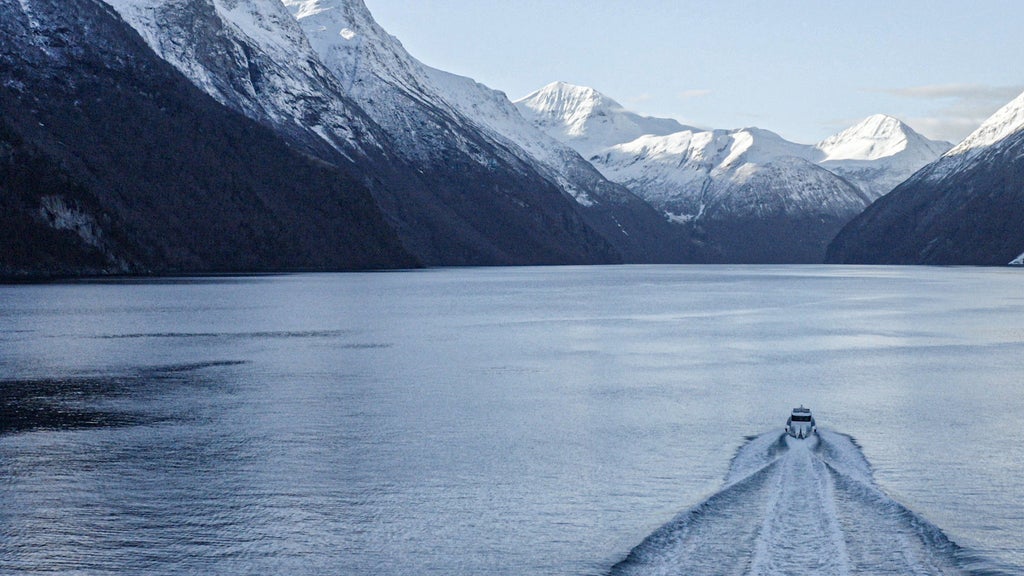 Scenic Norwegian fjord cruise with luxurious yacht gliding past steep emerald cliffs, crystal-clear waters reflecting dramatic Nordic landscape