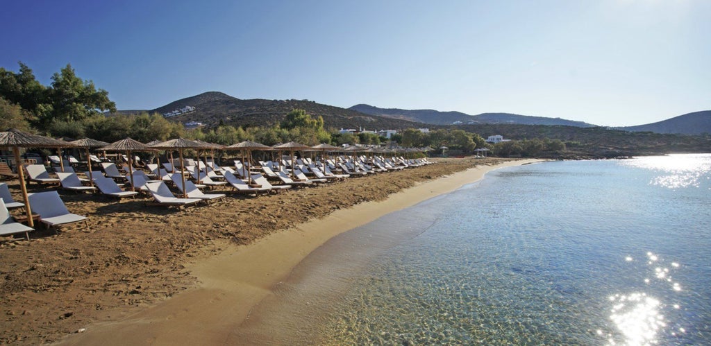 Elegant whitewashed luxury resort with infinity pools cascading down hillside, overlooking Mediterranean Sea at golden sunset hour