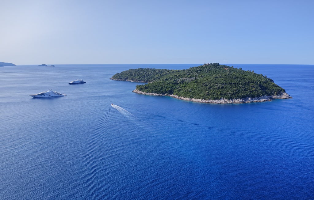 Elegant white sailboat cruising crystal-clear waters near lush Elafiti islands with rugged coastline and hidden coves in background