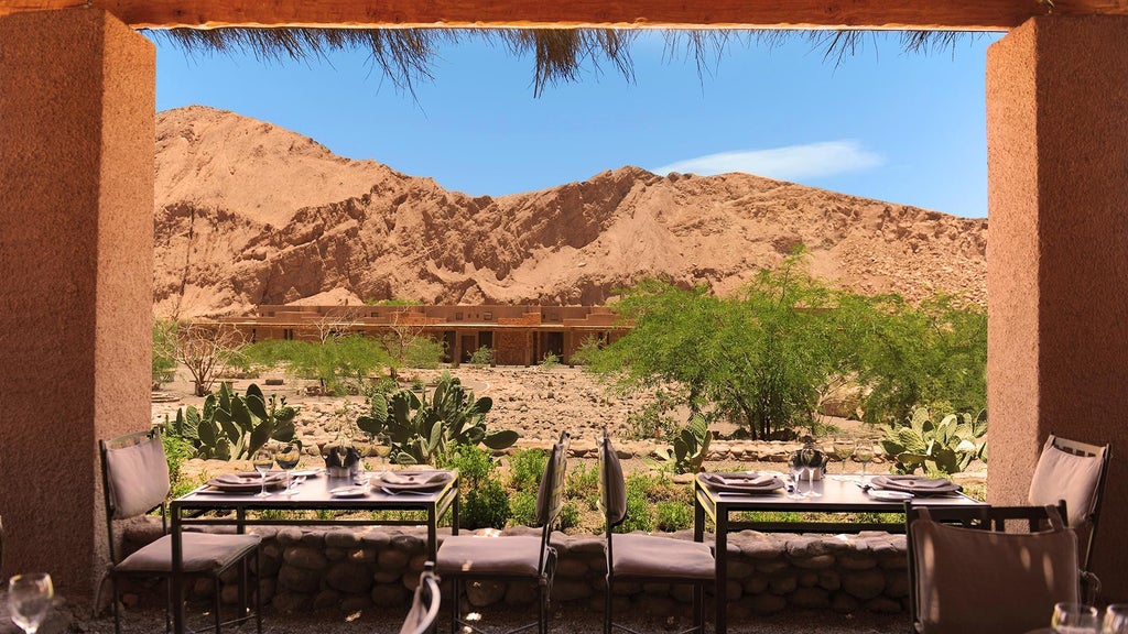 Luxurious desert lodge with adobe-style architecture nestled against red mountains, featuring a serene outdoor pool in the Atacama