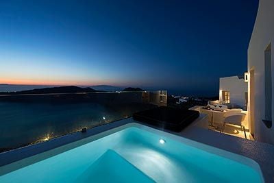 Luxurious Greek resort with infinity pool overlooking Aegean Sea, white-washed architecture, and lush Mediterranean landscape at sunset