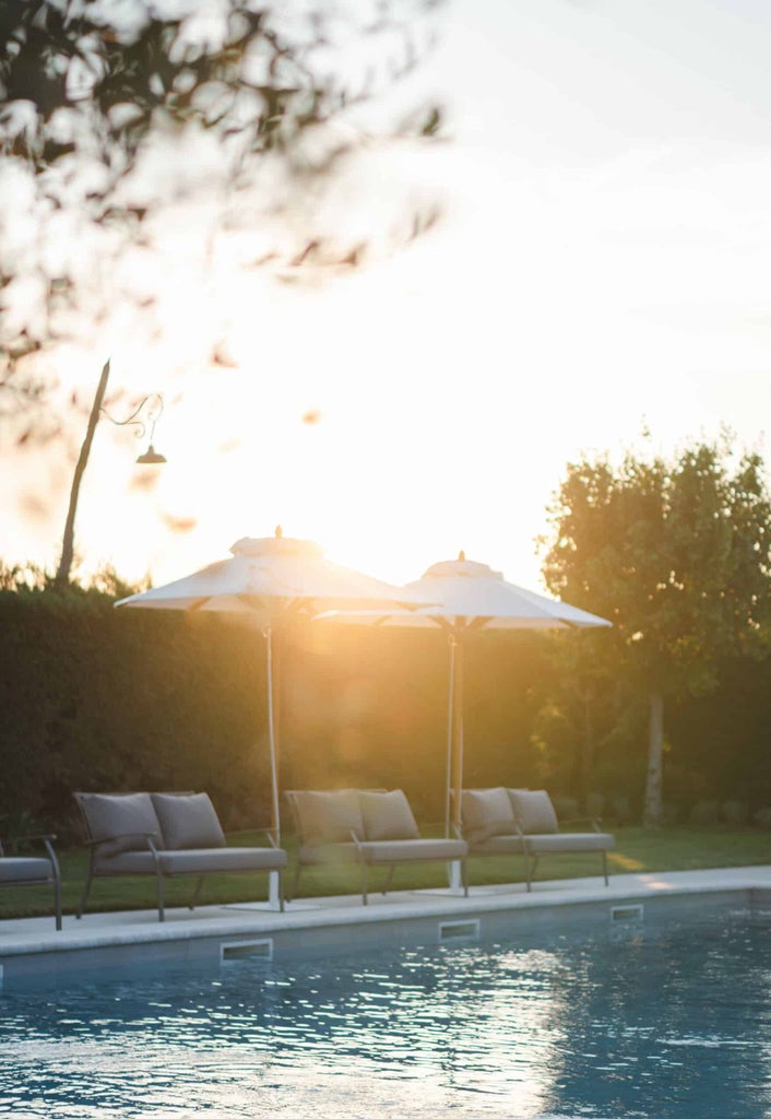 Elegant Tuscan hotel courtyard with stone walls, ivy-covered archways, manicured gardens and wrought iron furniture at dusk