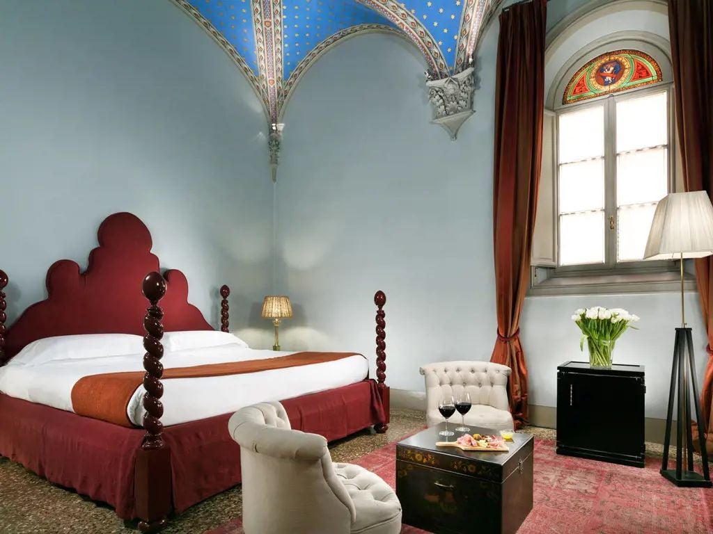 Elegant Tuscany hotel room with ornate antique furnishings, high ceilings, vintage chandelier, and luxurious cream-colored silk bedding in historic palazzo