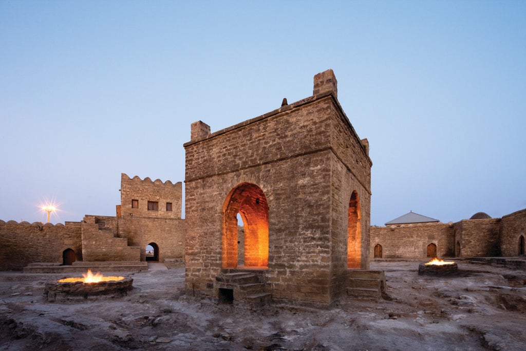 Majestic beige stone facade of Four Seasons Baku with ornate balconies, arched windows and grand entrance beneath a domed tower at dusk