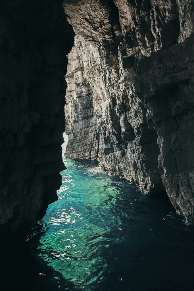 Private speedboat anchored in crystal-clear turquoise waters near secluded Croatian beach, white limestone cliffs rise from coastline