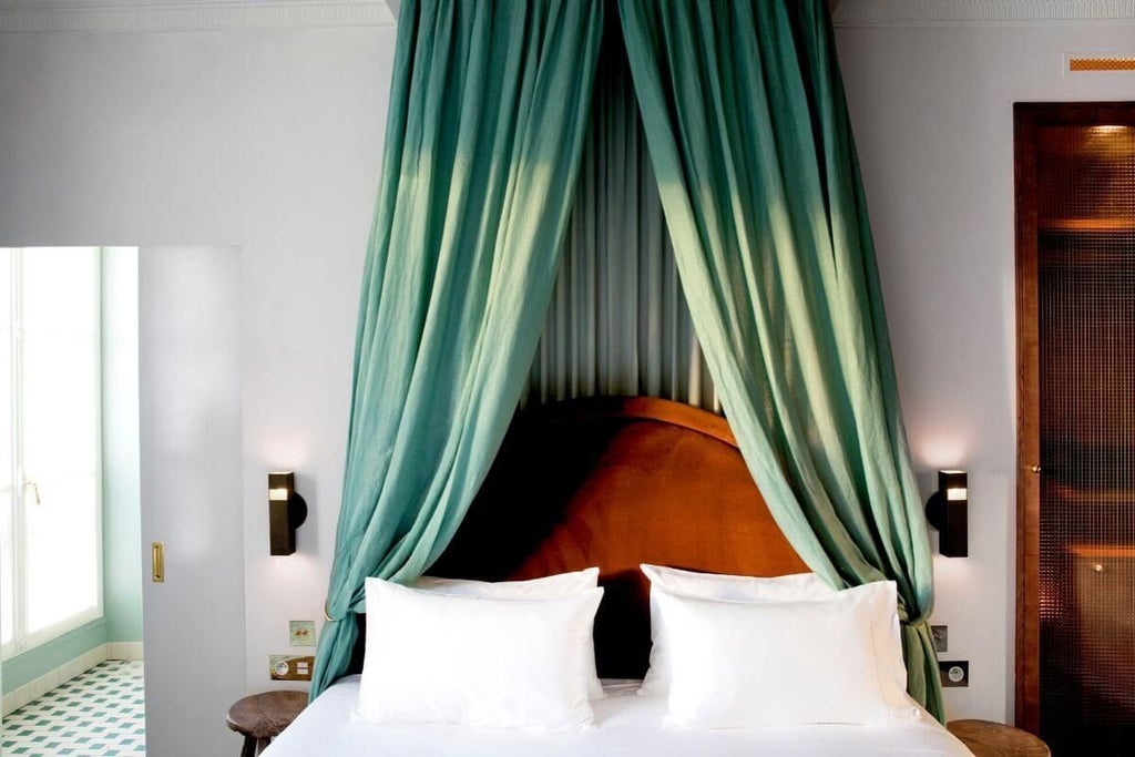 Elegant French hotel room with ornate chandelier, plush white bedding, soft neutral tones, vintage architectural details, and large arched window overlooking city street