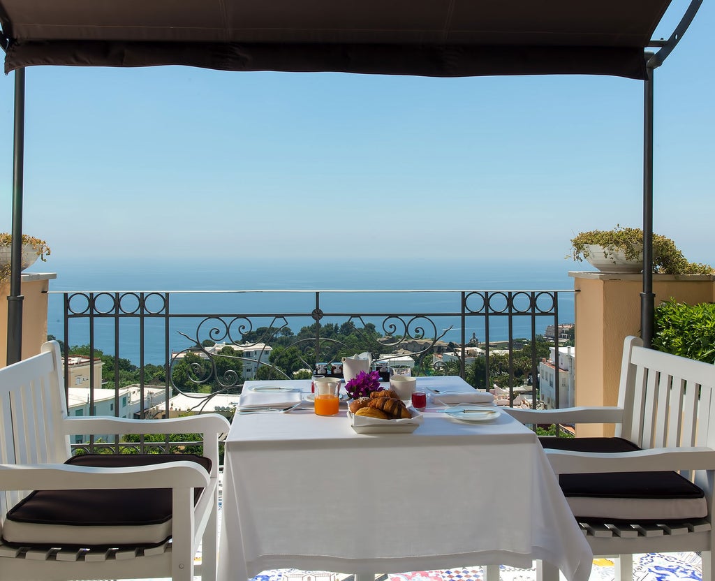 Elegant Mediterranean hotel exterior with white walls, arched windows, and lush gardens overlooking the Capri coastline at sunset