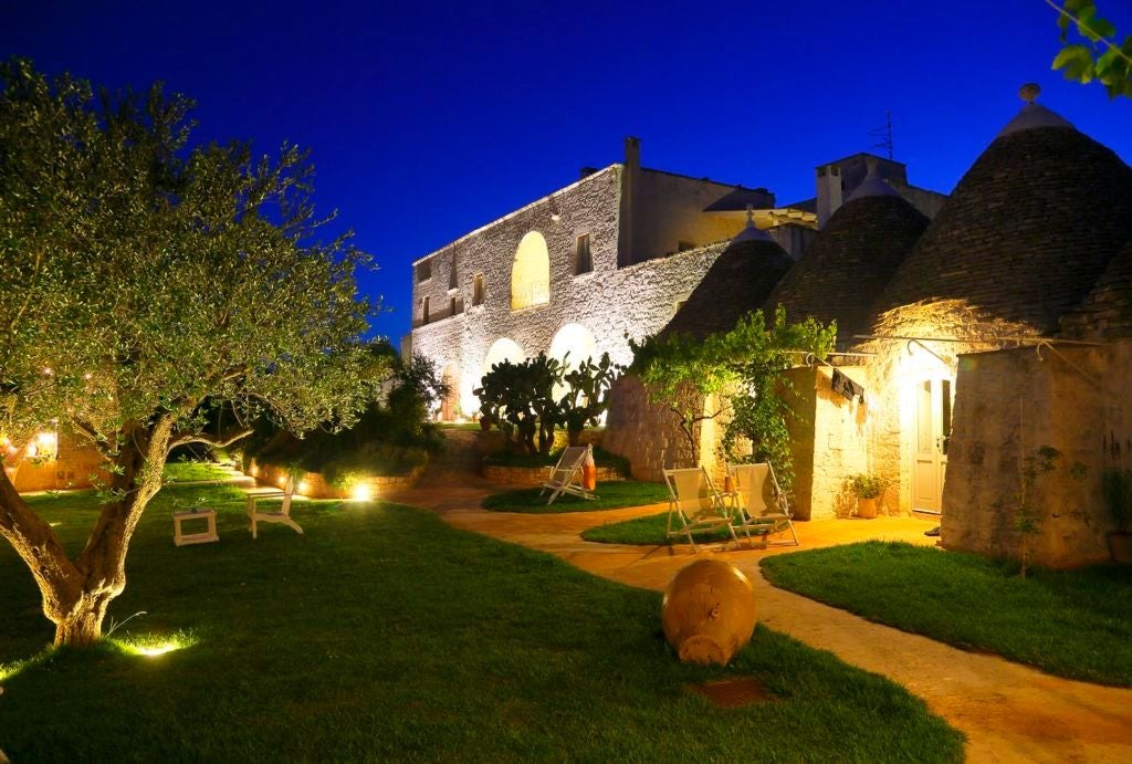 Rustic stone Apulian farmhouse with white-washed walls, surrounded by lush olive groves and azure sky, showcasing elegant Mediterranean luxury in Puglia, Italy