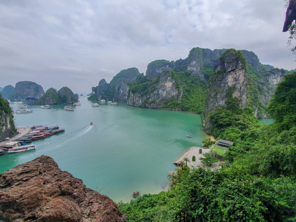 Luxury cruise ship anchored in Ha Long Bay, Vietnam, with traditional wooden junk boat design against emerald waters and limestone karsts