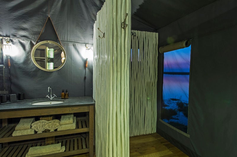 Elevated luxury tent on wooden deck overlooking African savanna, featuring private plunge pool and canvas walls at sunset