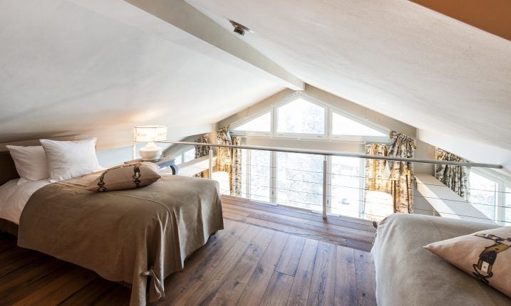 Elegant Swiss hotel suite with plush white bed, ornate crystal chandelier, and panoramic mountain view through floor-to-ceiling windows in soft neutral tones