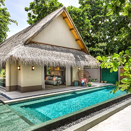 Luxury overwater villa with private infinity pool suspended above turquoise Maldivian lagoon, surrounded by lush palm trees and coral reefs