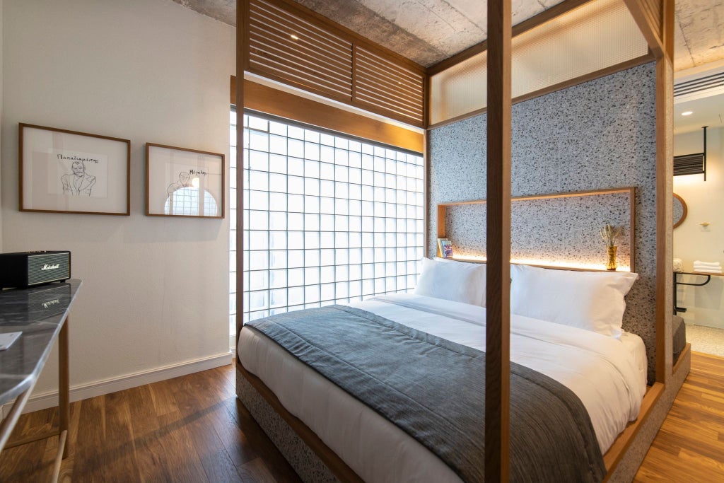 Spacious minimalist hotel room with wooden floors, white walls, plush king bed, and large windows overlooking scenic Athens urban landscape at golden hour