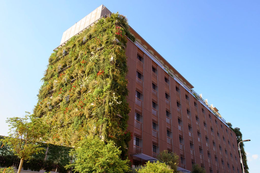 Modern luxury hotel exterior with vertical garden walls, sleek glass facade, and tiered balconies overlooking Milan's bustling cityscape