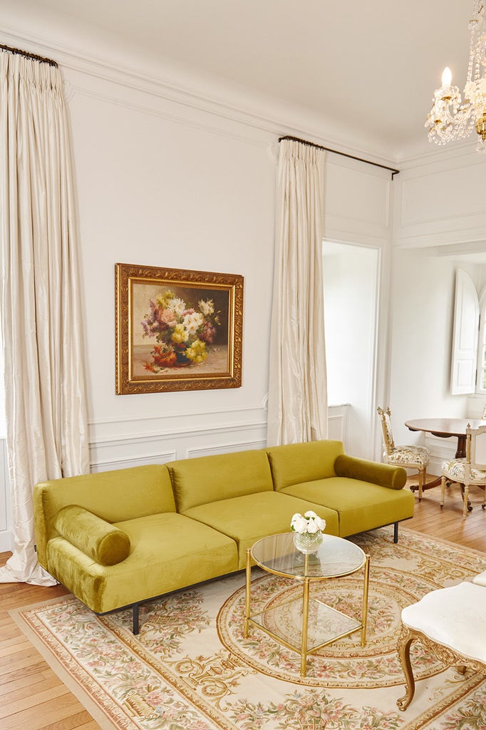 Elegant corner king room with ornate crown molding, crystal chandelier, garden views through tall French windows, and period furnishings