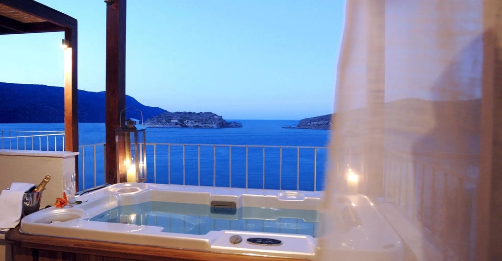 Luxurious family suite with outdoor jacuzzi overlooking the Aegean Sea, featuring elegant white decor and panoramic views of Elounda's scenic coastline