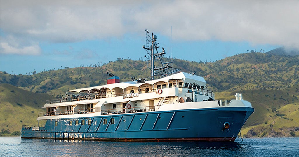 Luxurious white expedition yacht anchored in turquoise Indonesian waters, with spacious decks and elegant design against tropical backdrop