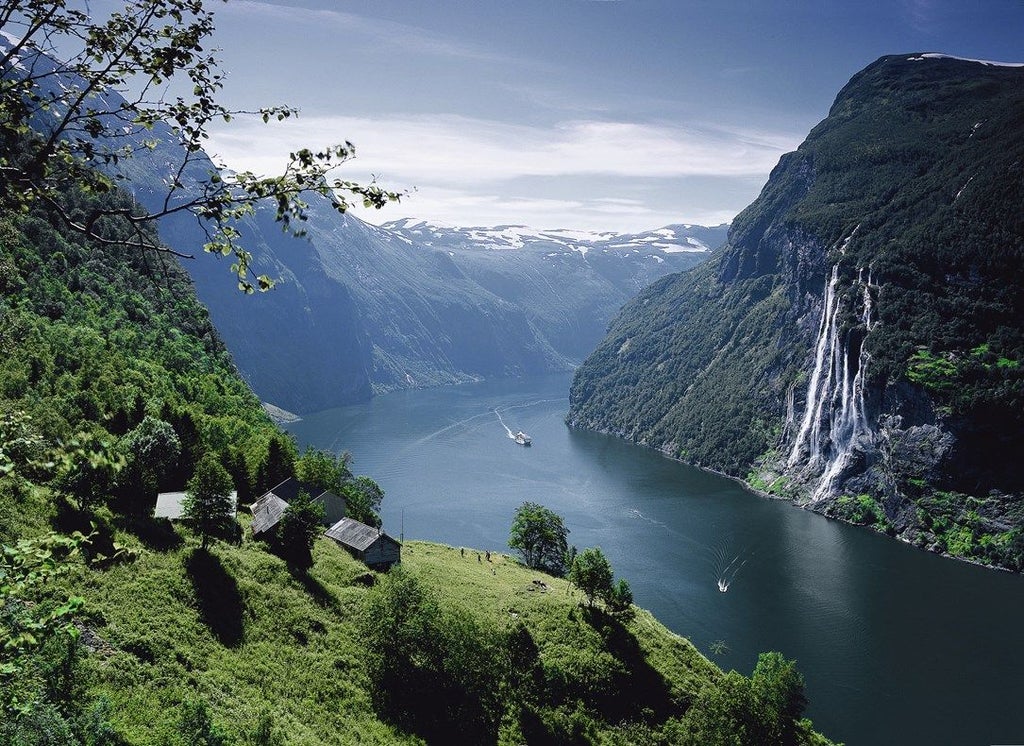 Sleek wooden boat cruises along emerald fjord waters beneath dramatic cliffs, offering intimate views of Norway's pristine wilderness