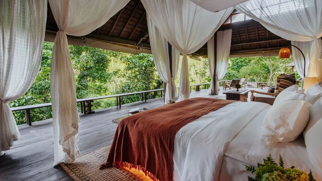 Luxury open-air villa in Bali rainforest with infinity pool overlooking lush jungle valley and distant mountain peaks at sunset