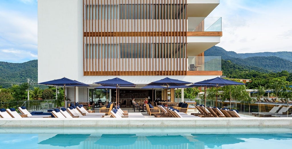 Oceanfront luxury hotel with infinity pool overlooking mountains and boats in Angra dos Reis, white modern architecture at sunset