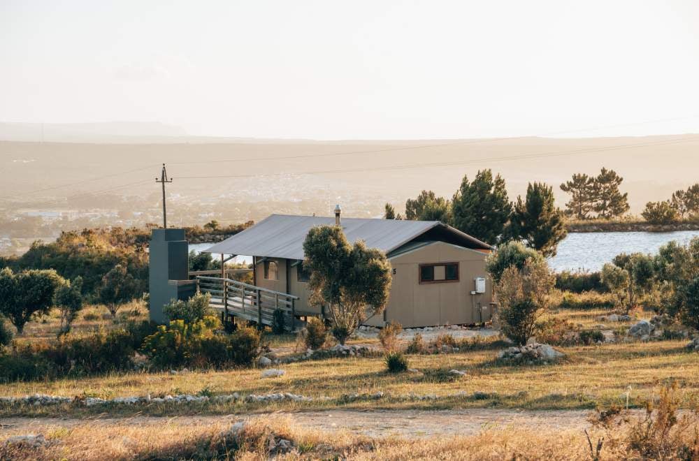 Luxury glamping tent with private deck overlooking rolling vineyards and Stanford Hills mountains at sunset, soft golden lighting