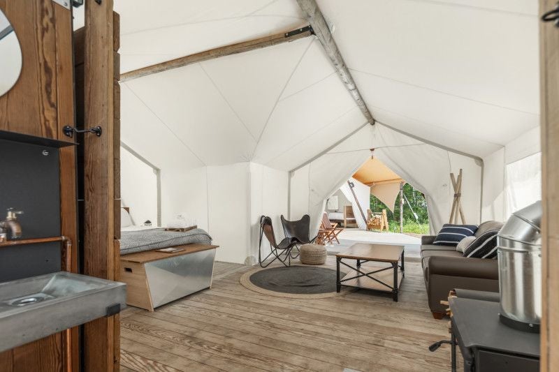 Spacious safari-style canvas tent suite with wooden bed, large windows overlooking scenic desert landscape at Under Canvas near Zion National Park