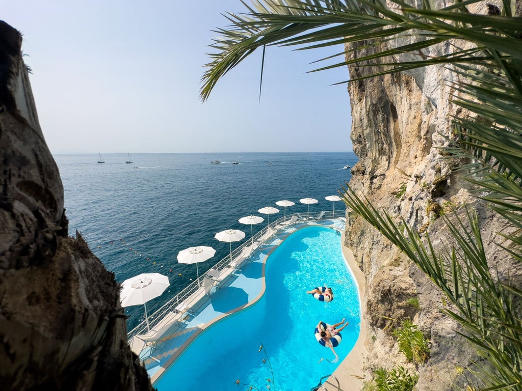 Elegant Mediterranean hotel perched on Amalfi cliffs with infinity pool overlooking turquoise waters and dramatic coastline views