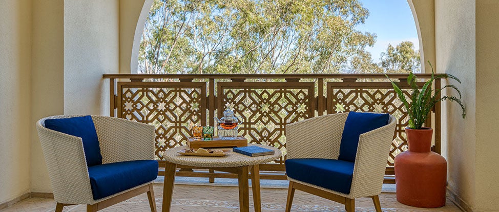 Elegant hotel room with forest views featuring a king bed, ornate Moroccan lamps, plush seating area and richly patterned textiles