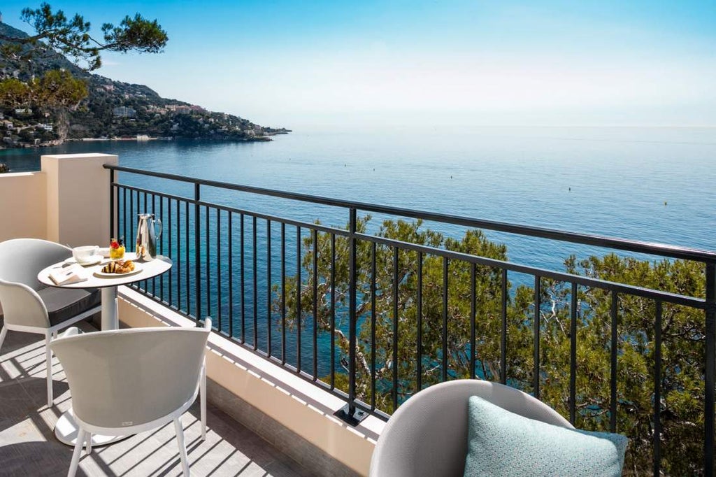 Luxurious hotel built into Mediterranean cliffside, featuring infinity pool overlooking azure waters and private coastal gardens