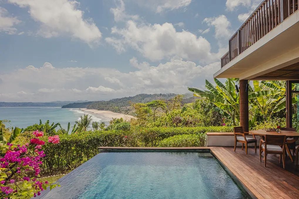 Luxurious open-air bedroom with traditional thatched roof, panoramic ocean views, and elegant wooden furnishings at NIHI Sumba resort, Indonesia