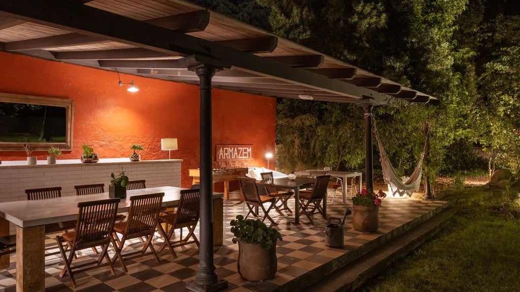 Elegant rustic Portuguese country house with stone walls, terracotta roof, surrounded by lush green gardens and rolling vineyard landscape at sunset.