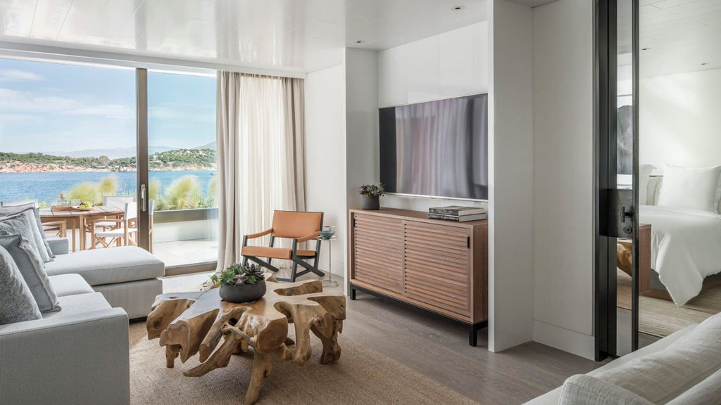 Elegant hotel suite with floor-to-ceiling windows overlooking Aegean Sea, modern furnishings and white marble bathroom with soaking tub