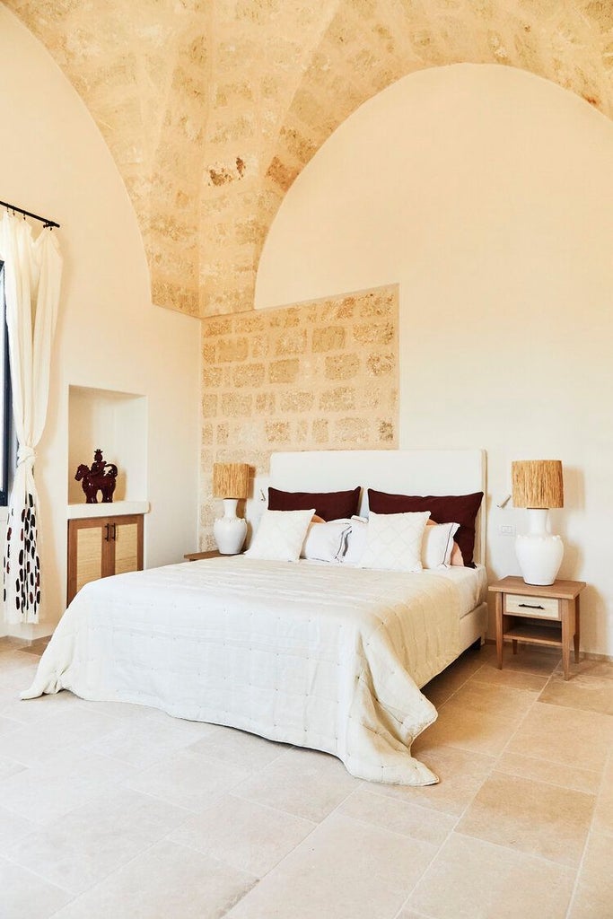 Elegant stone-walled tower suite with arched window, rustic wooden furnishings, and soft neutral palette overlooking scenic Italian countryside at Masseria Calderisi