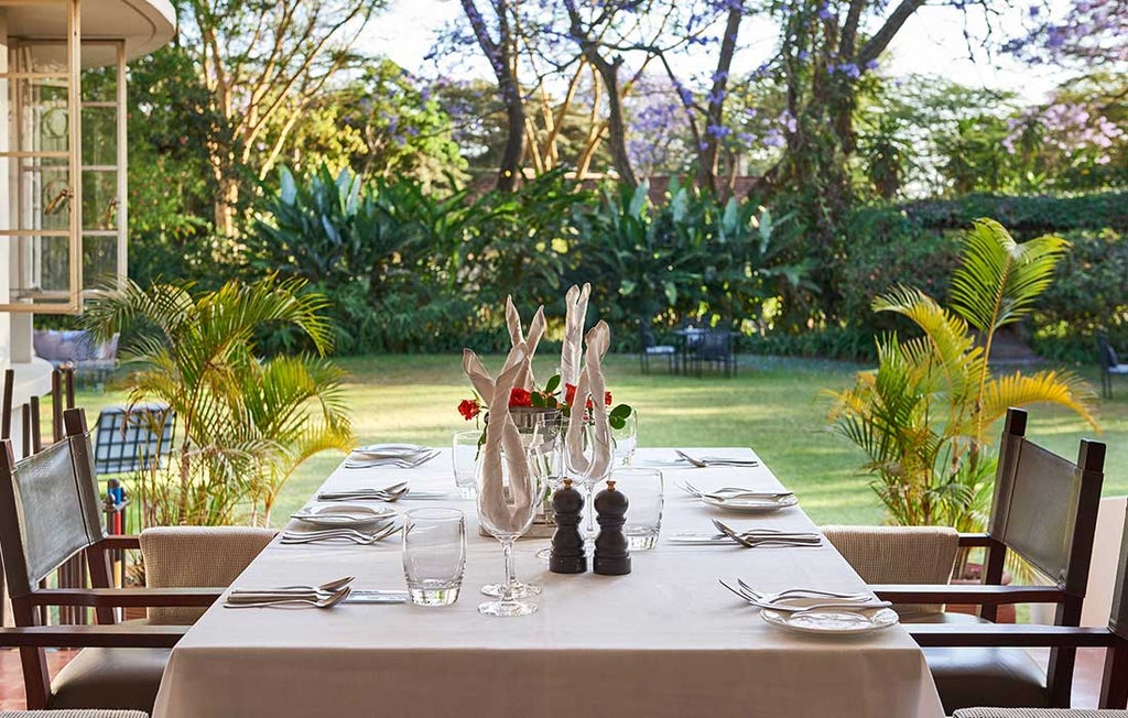 Elegant safari lodge cottage with thatched roof set amid lush tropical gardens, Mount Meru visible in misty background, luxury veranda