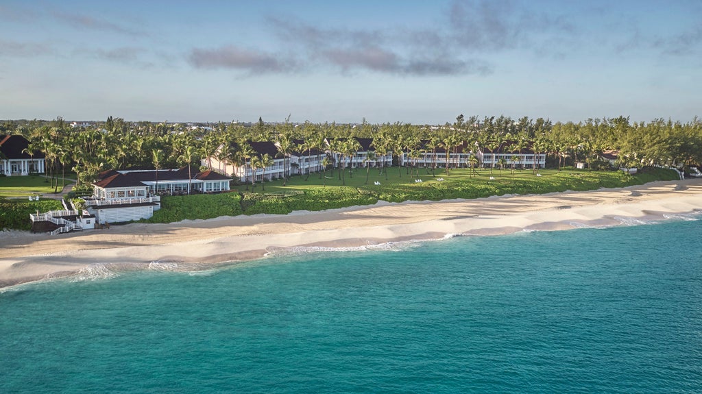 Oceanfront luxury resort with white sand beach, infinity pools, and swaying palm trees against turquoise Caribbean waters at sunset