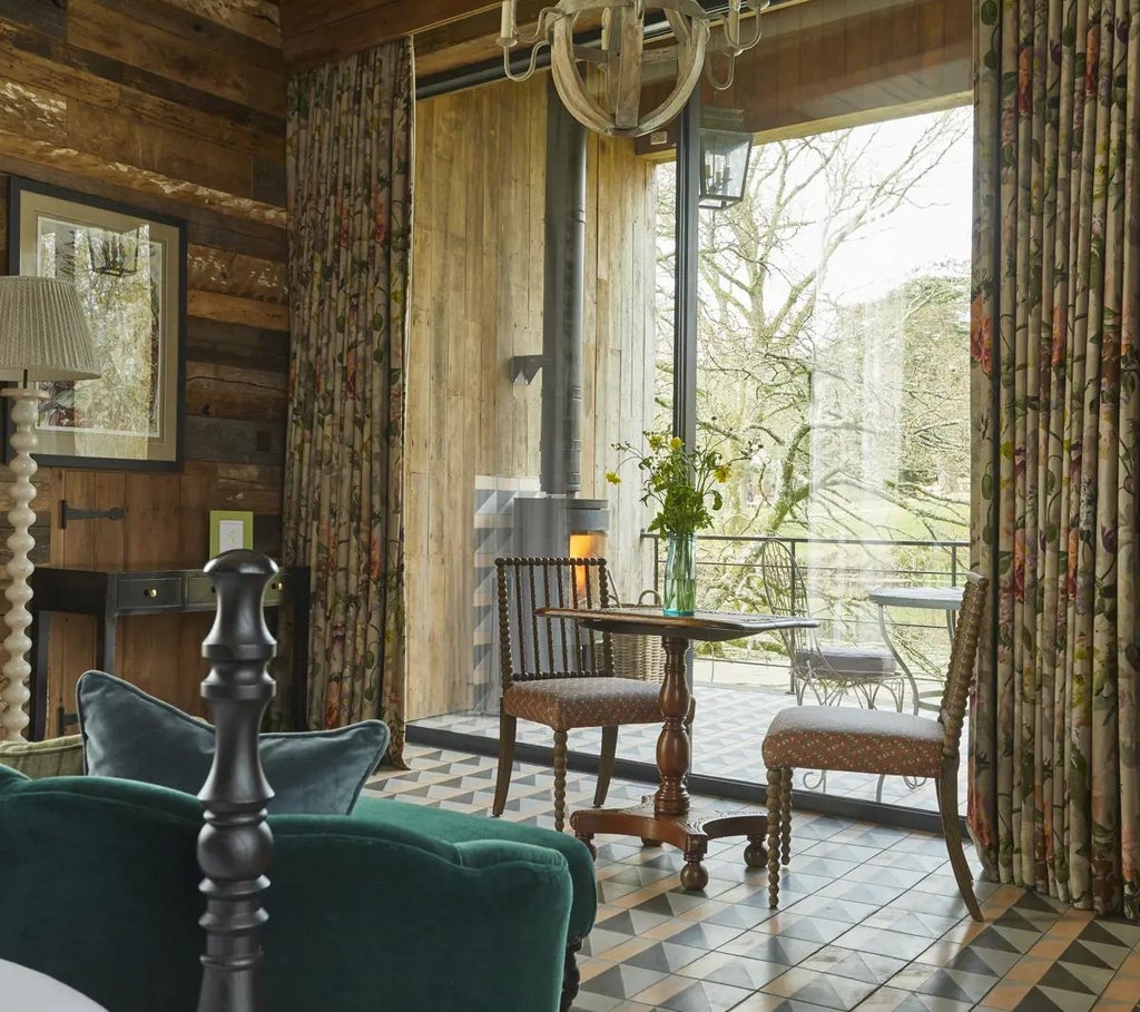 Luxurious forest cabin room at Lime Wood, featuring rustic wood paneling, elegant furnishings, and panoramic woodland views through large windows