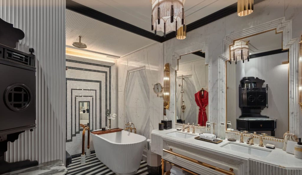 Elegant opera-themed hotel suite with white marble bathroom, clawfoot tub, ornate gold fixtures, and French colonial-style furnishings