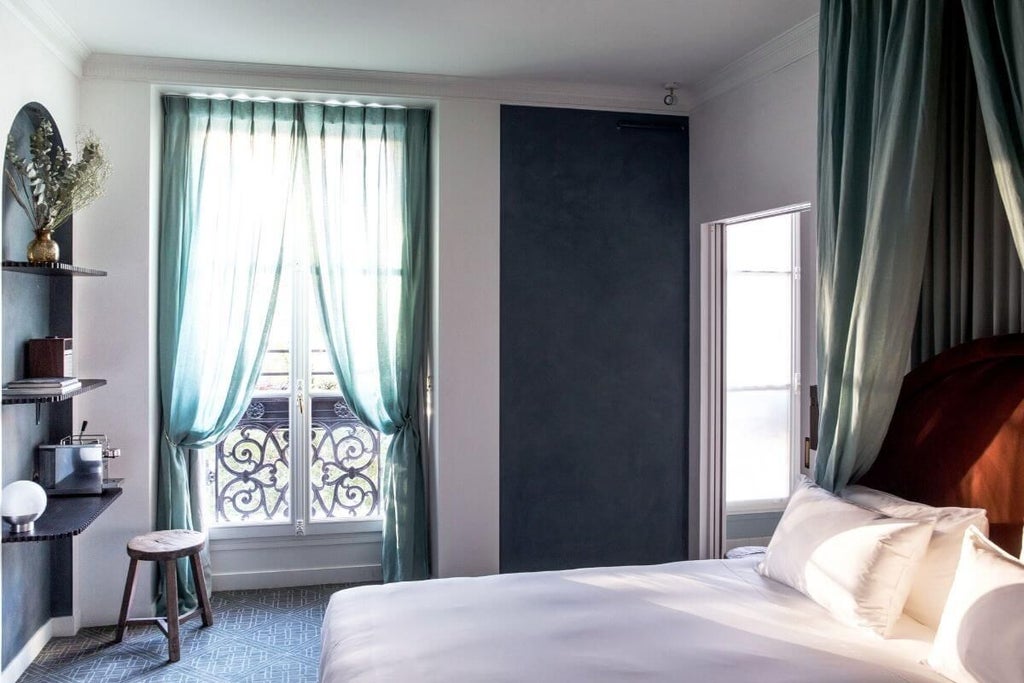 Elegant French hotel room with soft cream walls, ornate golden-framed mirror, luxurious white bedding, and vintage parisian architectural details