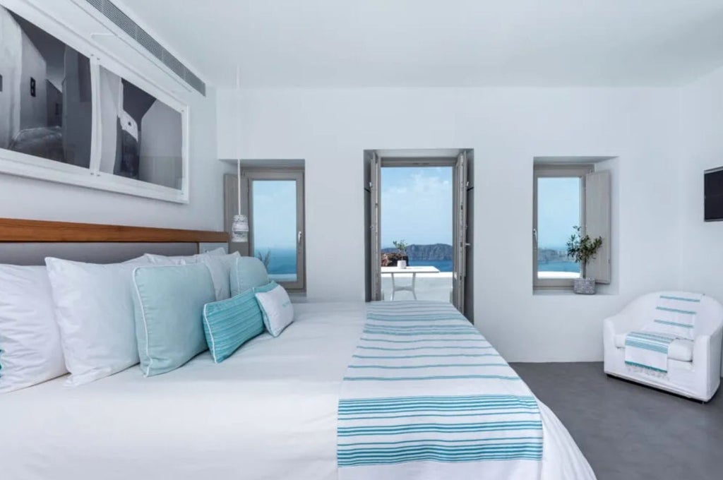 Elegant deluxe hotel room with white marble floors, king bed draped in crisp linens, and a private balcony overlooking the Aegean Sea