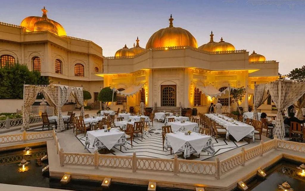 Ornate Indian palace hotel with golden domes and arches overlooking Lake Pichola, featuring manicured gardens and tranquil water pools