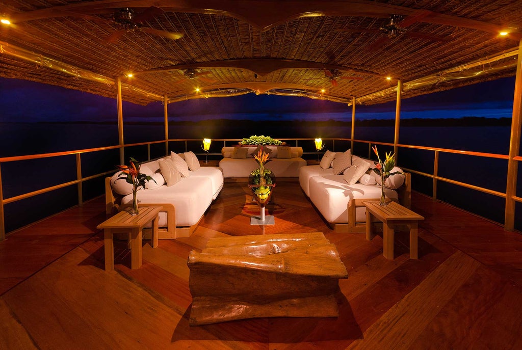 Luxurious riverboat cruise ship Delfin Amazon with wooden deck and outdoor lounge area sailing through lush Peruvian rainforest waters