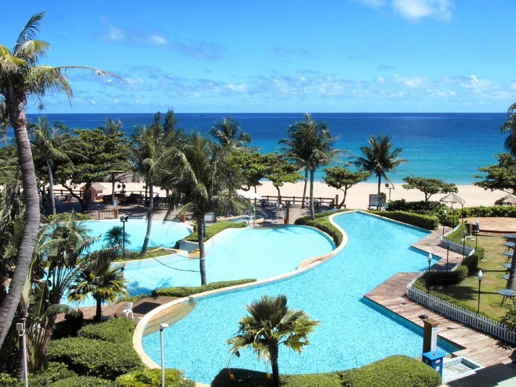 Elegant beachfront resort with modern white architecture, infinity pool overlooking turquoise ocean, and swaying palm trees at sunset