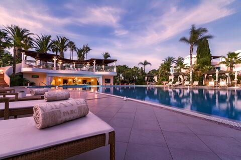 Luxurious oceanfront resort with white Mediterranean architecture cascading down cliffs, featuring lush gardens and infinity pools overlooking sea