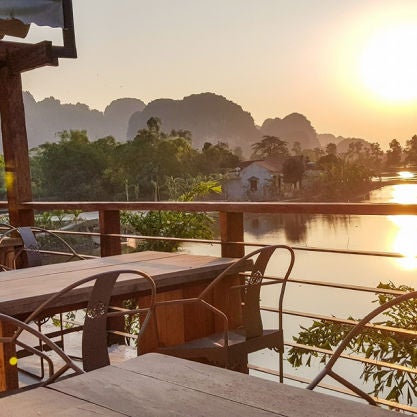 Luxurious bungalows with thatched roofs nestled among lush gardens and limestone mountains in Vietnam, reflecting in calm waters at sunset